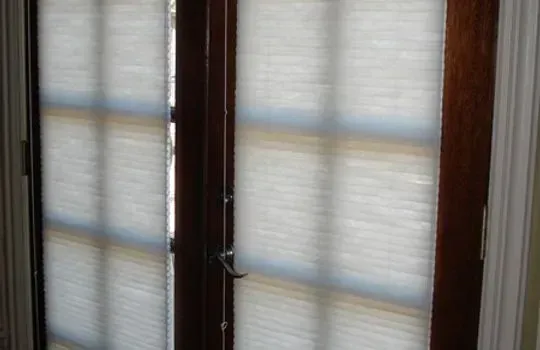 Two windows with light-filtering cellular shades, set in a dark wood frame.