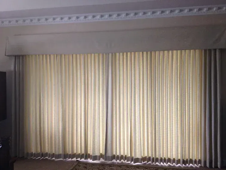 Light beige pleated curtains with a matching valance above a window.