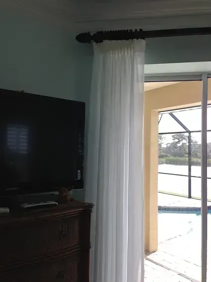 White sheer curtain next to a glass sliding door, mounted on a dark brown curtain rod.