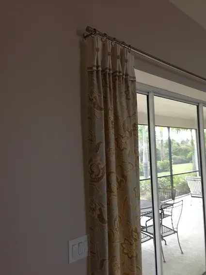 Beige patterned curtain on a silver rod, covering a sliding glass door.