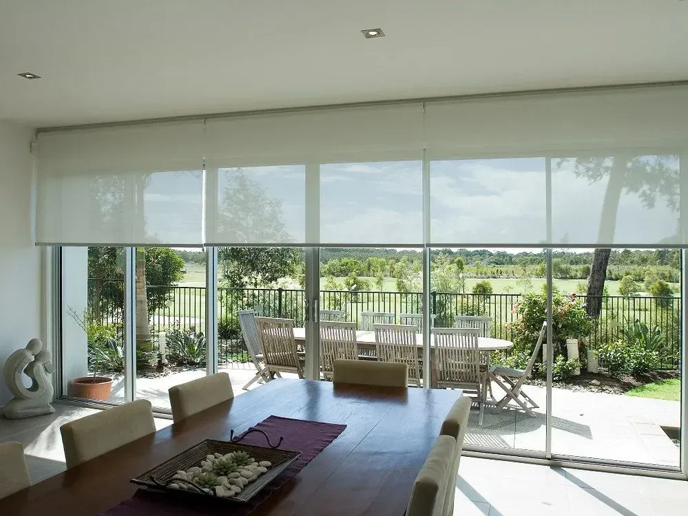 Dining room with large windows overlooking a patio with a dining table and a green landscape.