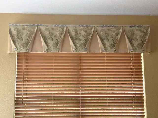 Window with beige blinds and a decorative valance with pleated fabric.