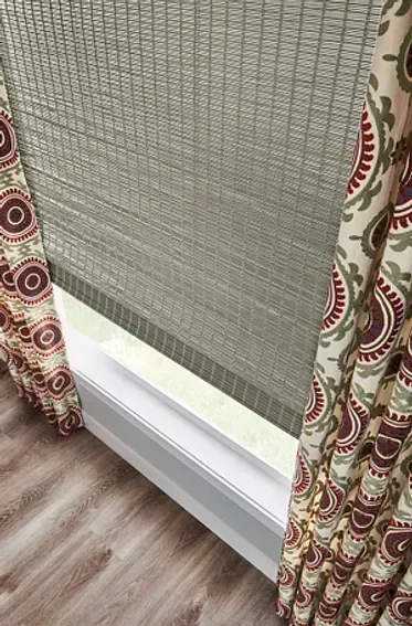 Window with tan woven shade and patterned curtains.