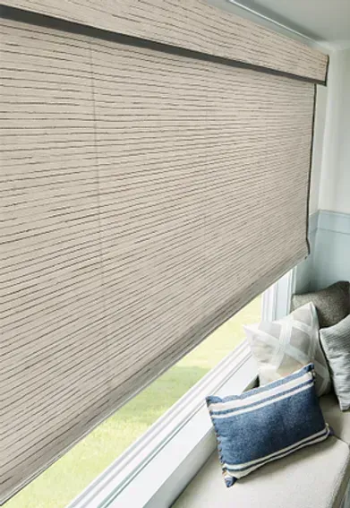 Roller shade over a window in a window seat with pillows. Beige and blue tones.