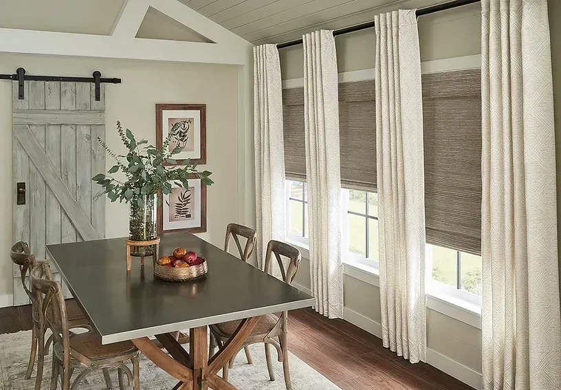 Dining room with dark table, wooden chairs, barn door, and three windows with blinds and white curtains.
