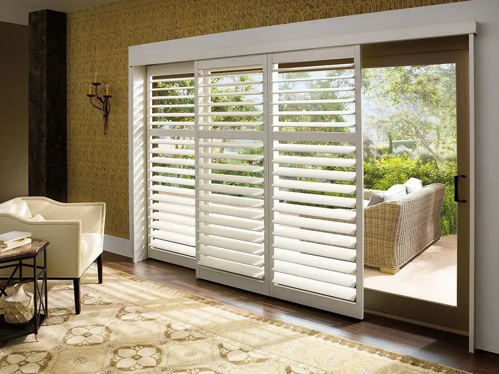 Sliding glass doors with white shutters, leading to an outdoor patio with wicker furniture.