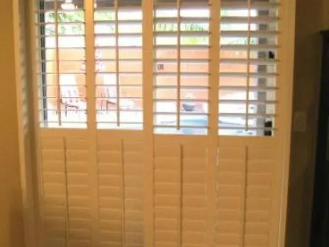 White shutters cover a window; a glimpse of a patio with furniture is visible through the open slats.