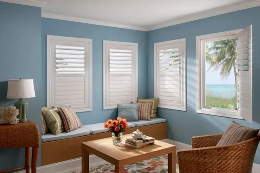 Cozy living room with blue walls, white shutters, window seat, and ocean view.