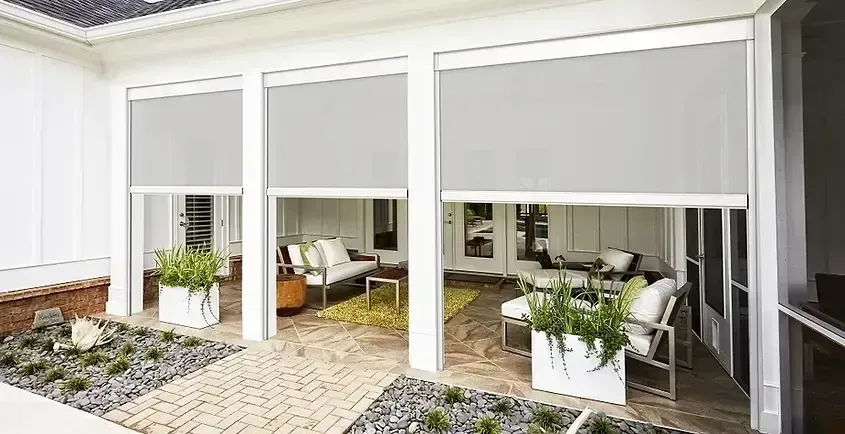 Three gray outdoor roller shades partially lowered on a patio.