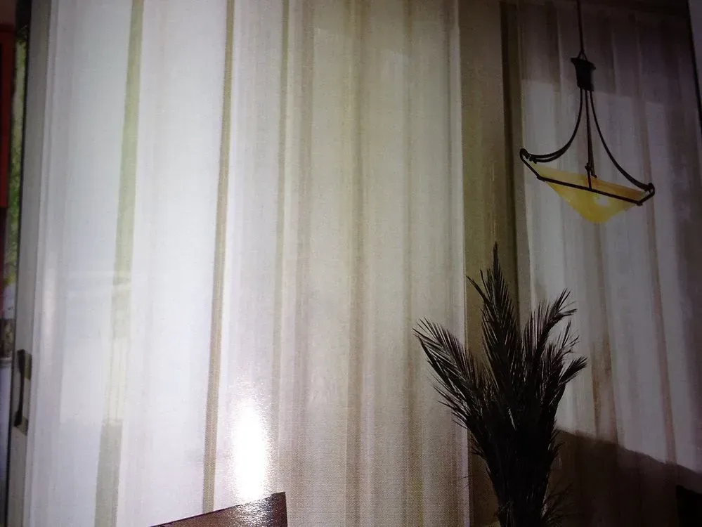 Cream-colored sheer curtains in a room with a decorative hanging light and a plant.