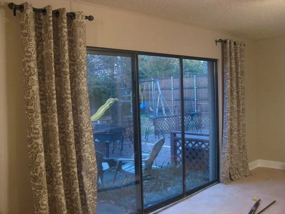 Curtains frame a sliding glass door overlooking a backyard with a playground.