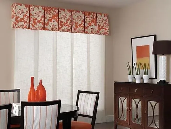 Dining room with floral valance, sheer panels, orange accents, and dark wood furniture.