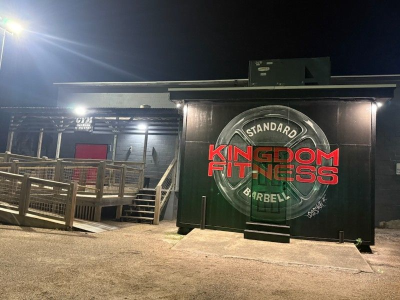 Kingdom Fitness barbell gym at night. Red and green sign. Wooden ramp and steps.