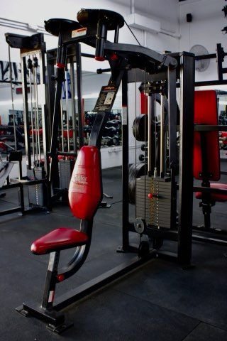 Weight machine with red seat in a gym. Black frame and weights are visible.