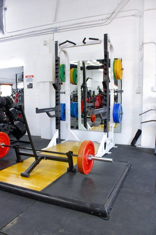 Weightlifting equipment: squat rack with plates in gym. Barbell loaded on platform.