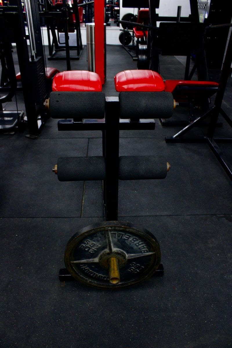 Weight machine in a gym. Black frame with red padding and a weight plate at the bottom.