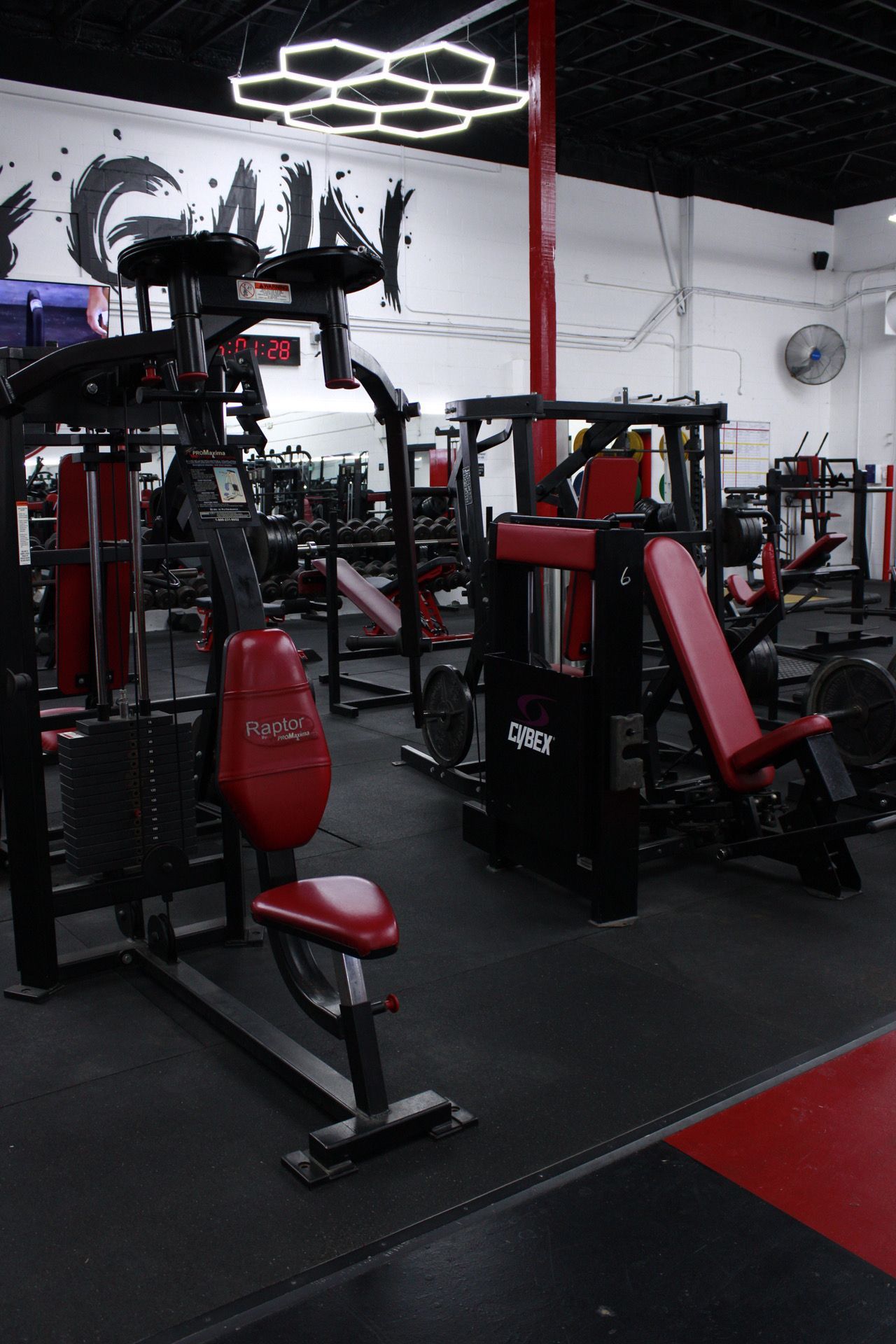 Gym interior with red and black exercise machines on a black floor.