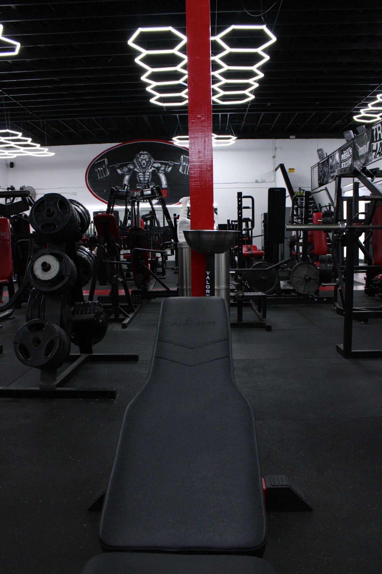 Interior gym with weights and equipment, viewed from a weight bench, red column in center.