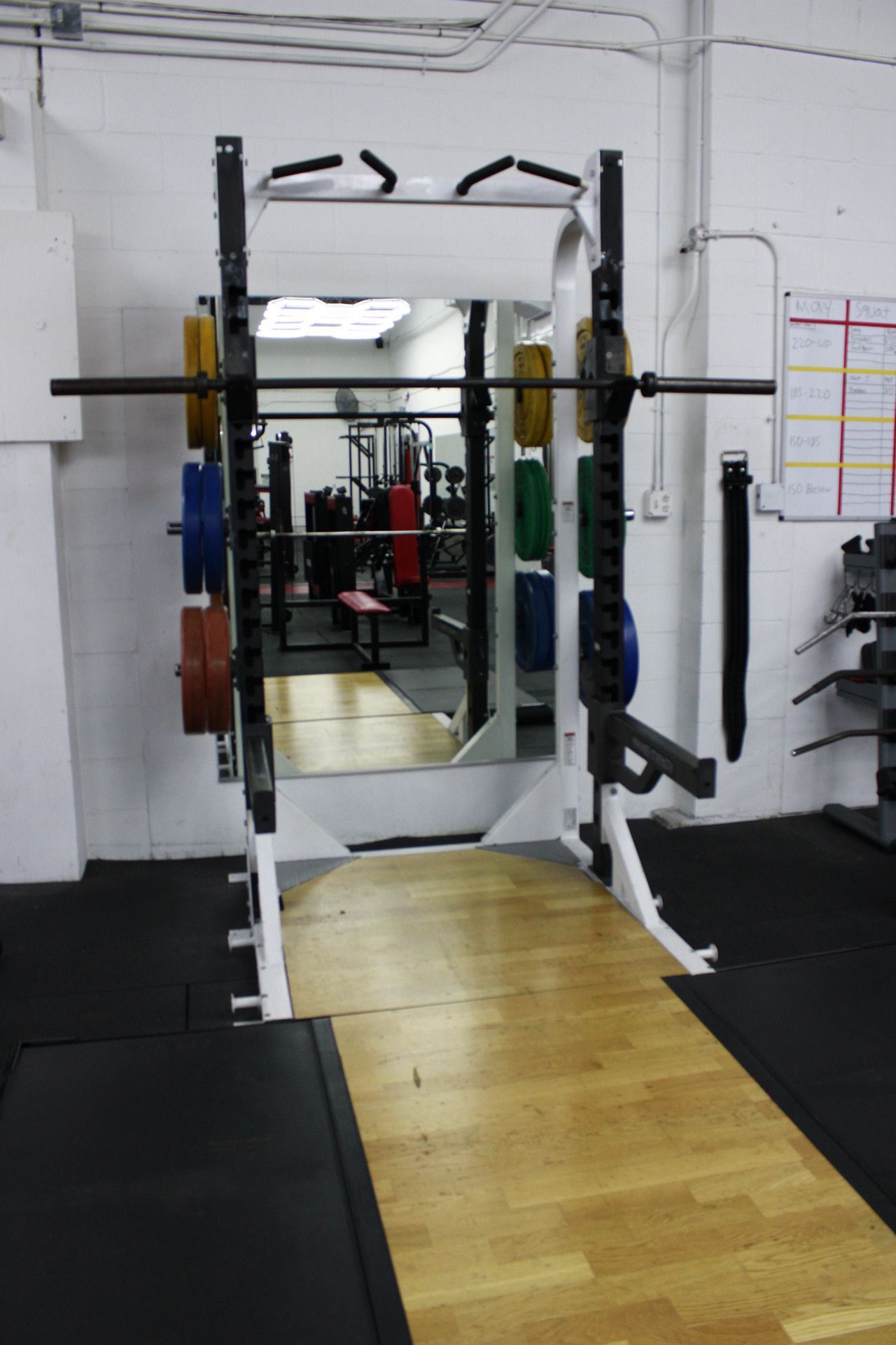 Squat rack with weights in a gym, with a mirror reflecting the equipment.