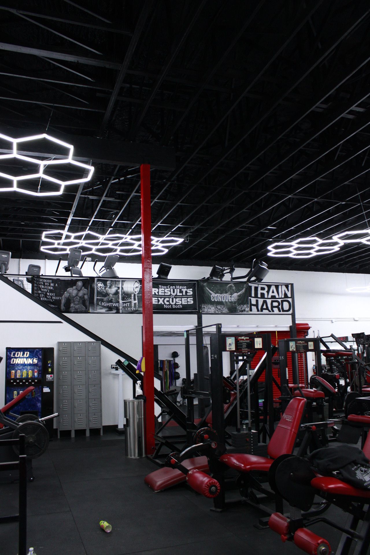 Gym interior with red and black equipment, honeycomb lights, and a sign that reads 