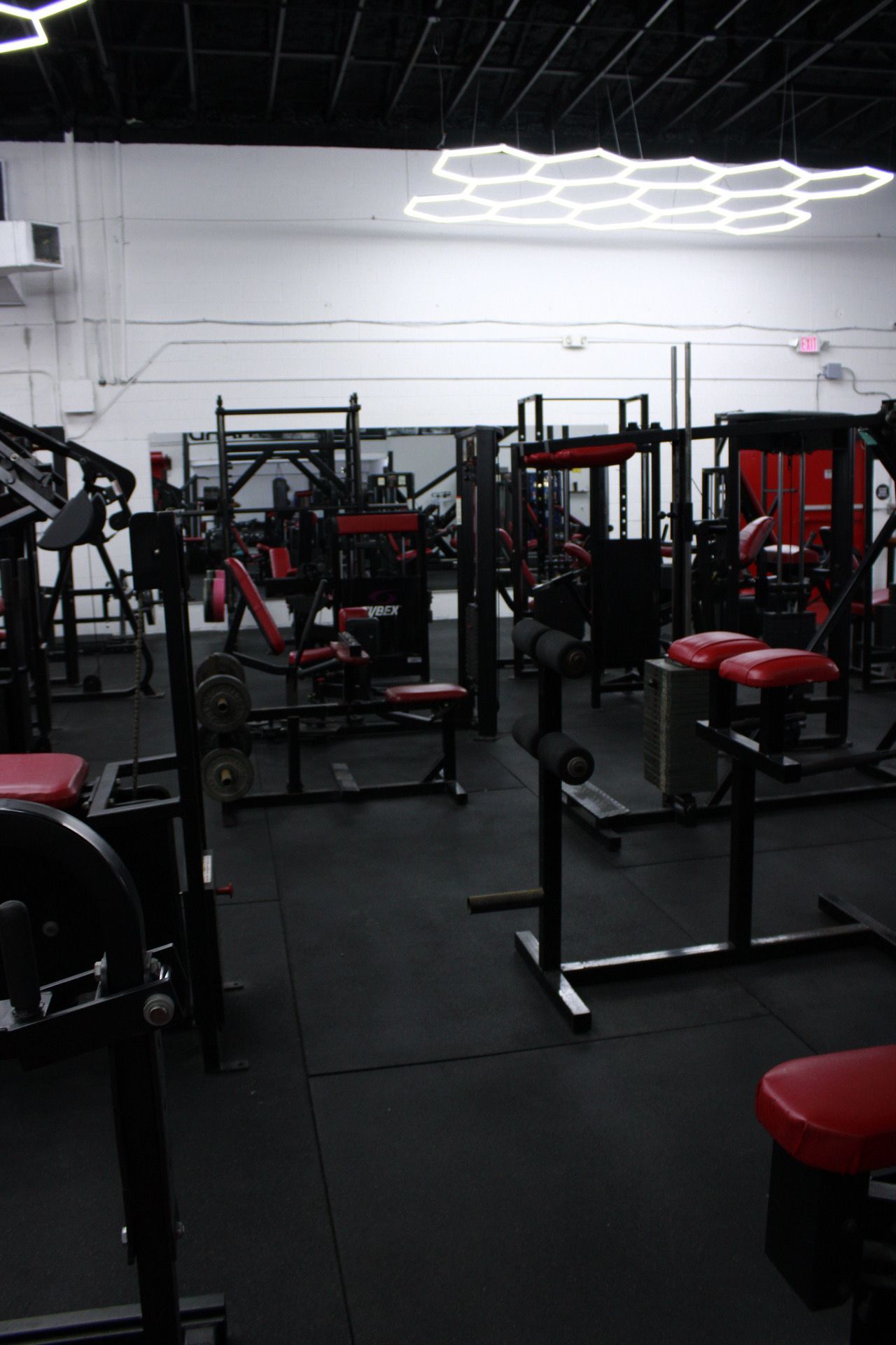 Gym interior with black and red exercise equipment on a black rubber floor, under white lighting.