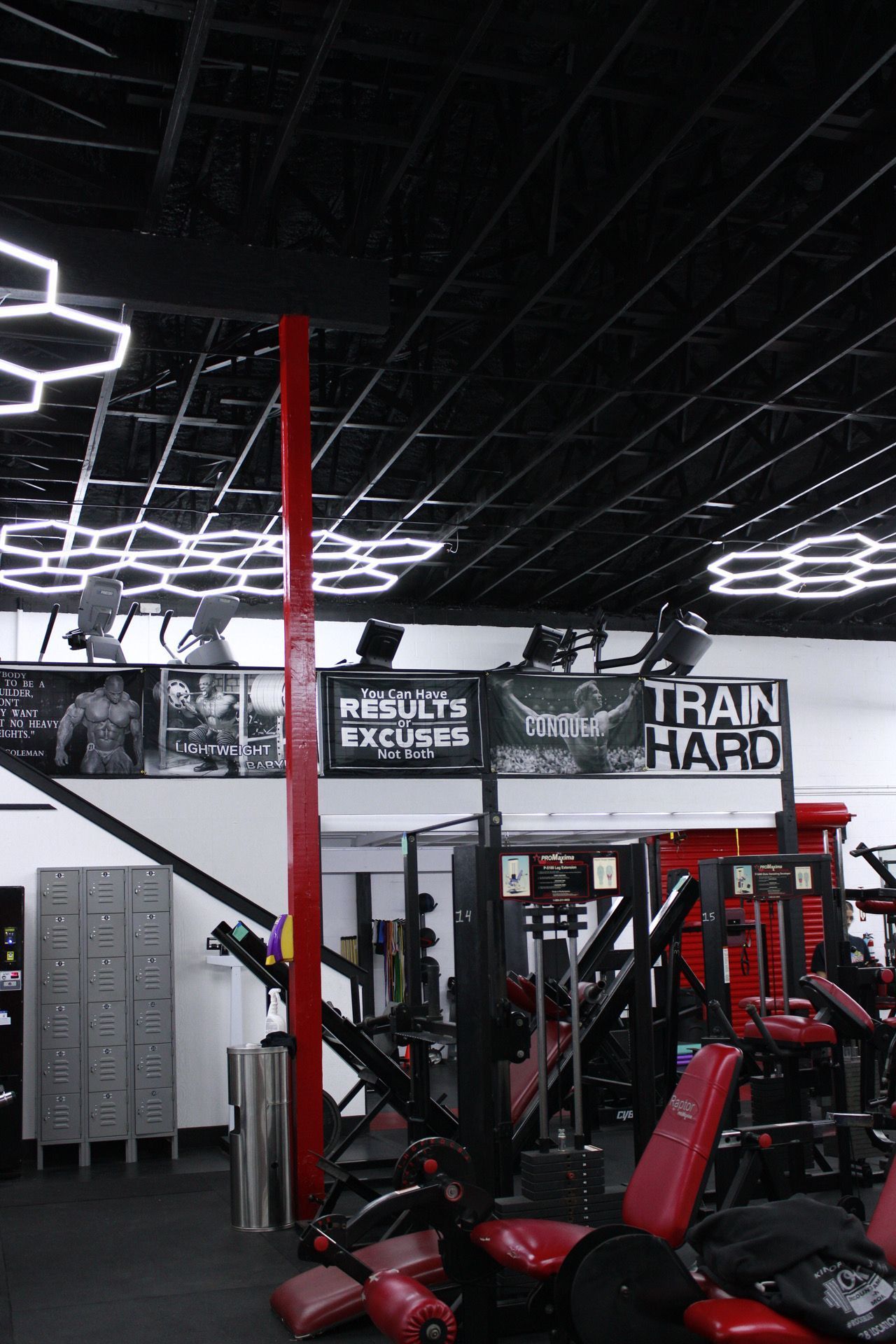 Gym interior with workout equipment. Black and red tones, hexagonal ceiling lights, 