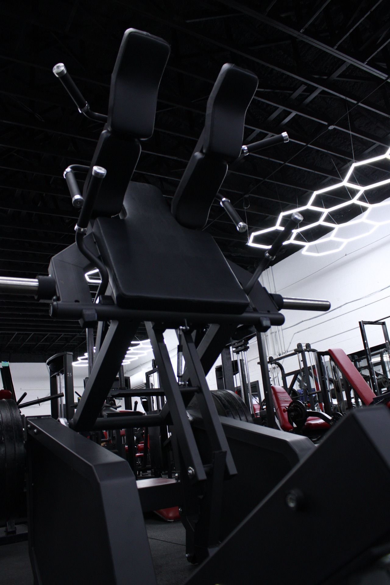 Black weight machine in a gym setting, with padding for shoulder and back support.