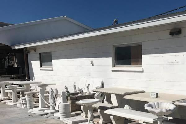 White building exterior with two windows. Marble tables and benches are in front of it.