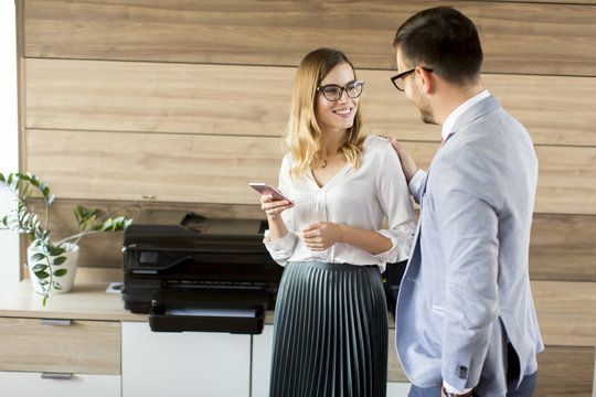 A man and a woman are standing next to each other in front of a printer.