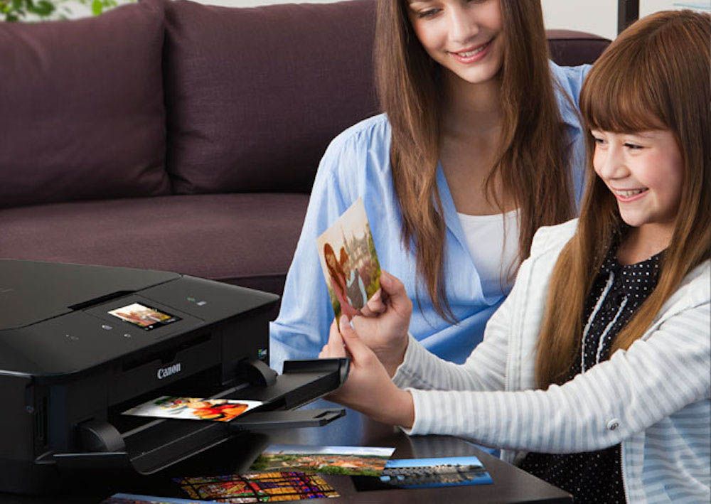 A woman and a little girl are looking at pictures in front of a canon printer.
