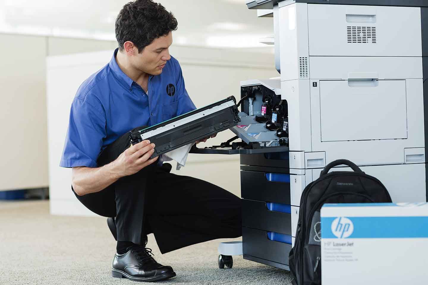 A man in a blue shirt is working on an hp printer