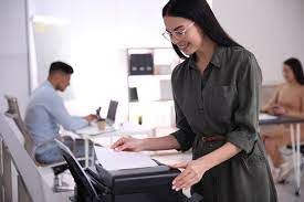 A woman is standing in front of a printer in an office.