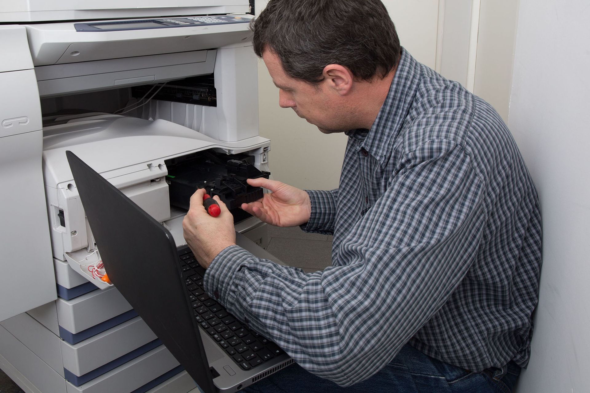 A printer technician is fixing a printer with a screwdriver