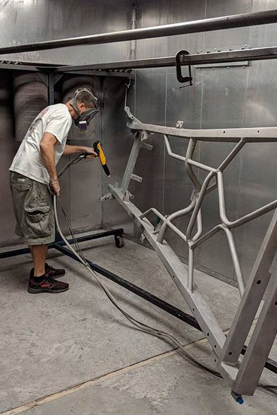 A man is painting a piece of metal in a room.