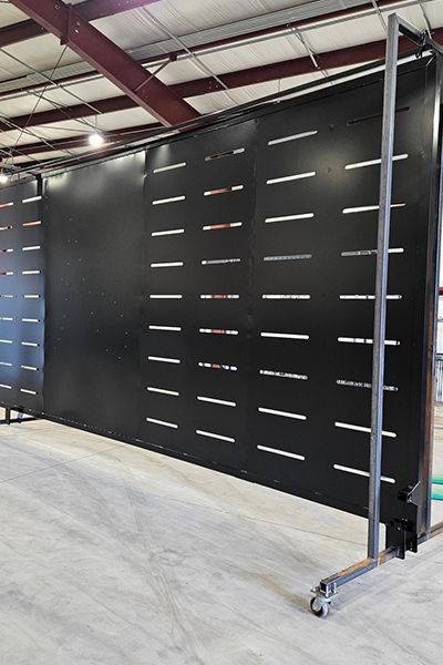 A large black metal wall with strip holes on it is sitting in a warehouse.