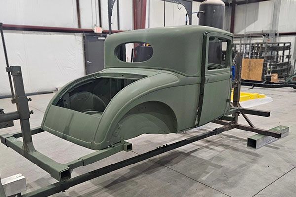 A green car body is sitting on a metal rack in a garage.