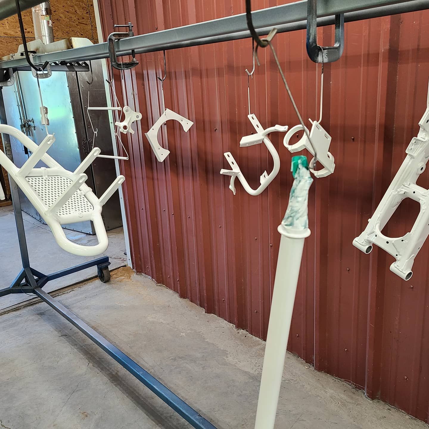 A bunch of white parts are hanging on a rack in front of a red wall.