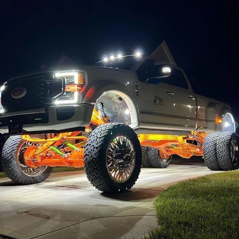 A truck with a lot of lights on it is parked in a driveway at night.