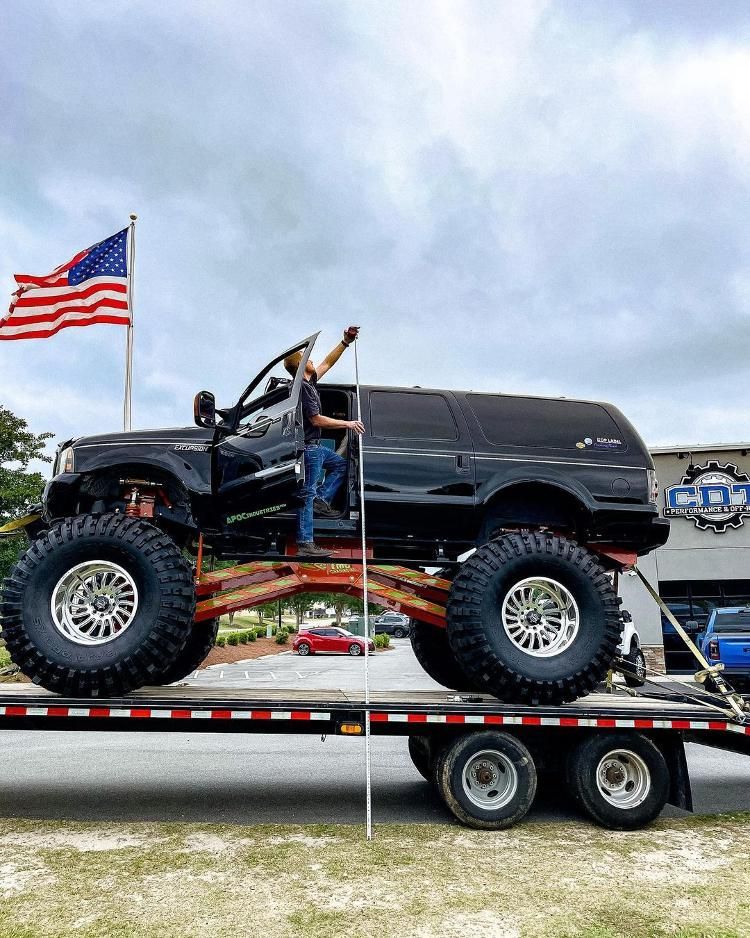 A man is standing on top of a truck on a trailer.