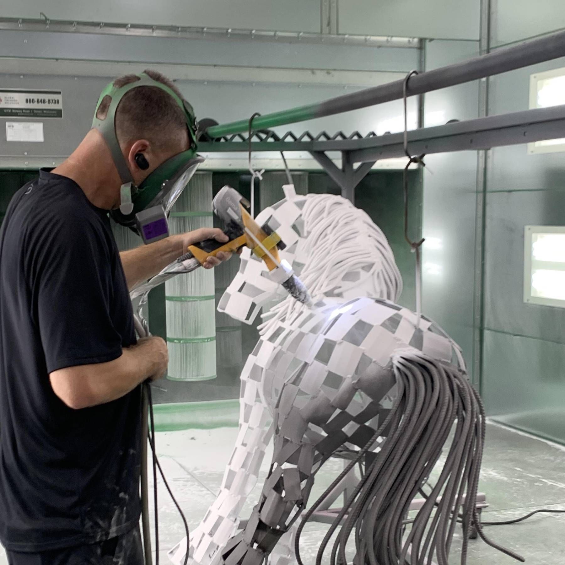 A man wearing a mask is working on a statue of a horse