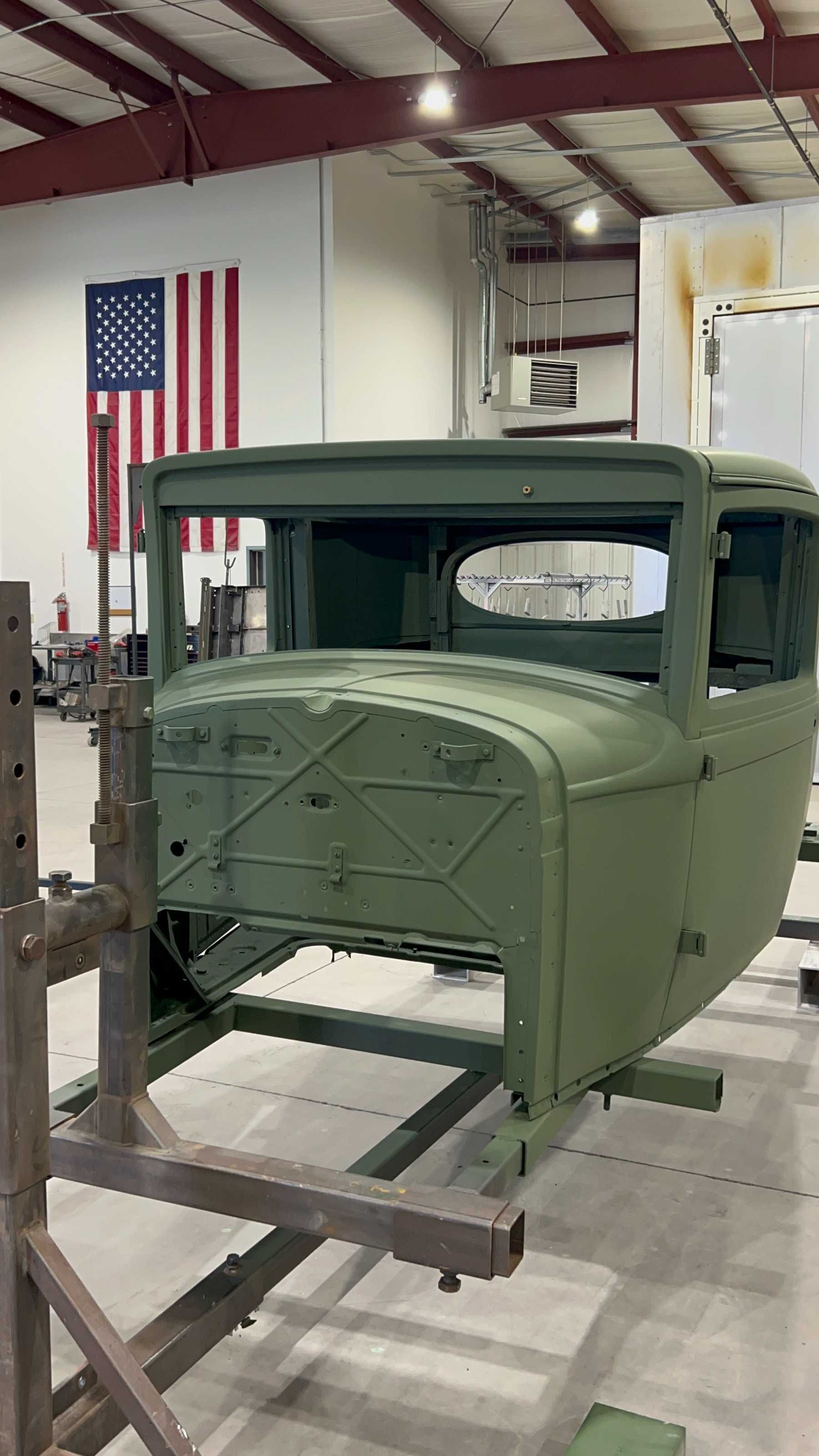 A green truck body is sitting on top of a metal stand in a garage.