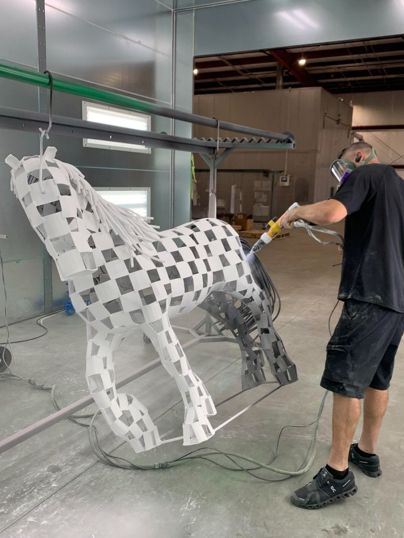 A man is painting a statue of a horse in a warehouse.