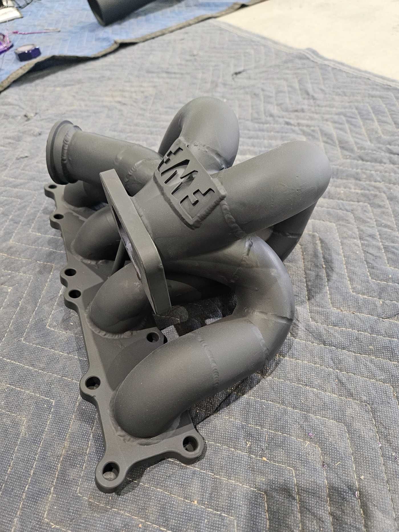A black exhaust manifold is sitting on top of a blue blanket.