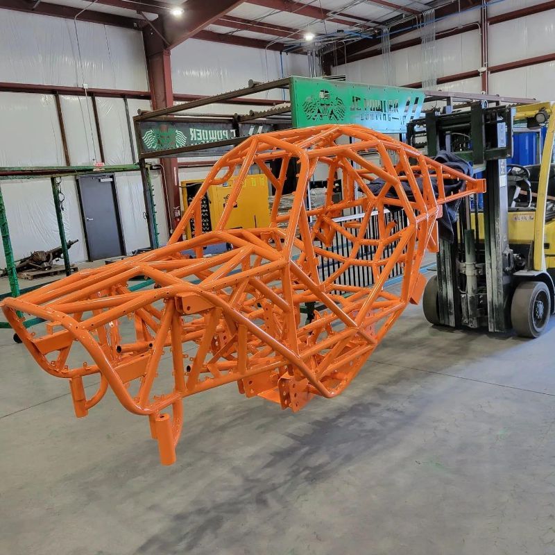 A forklift is carrying a large orange structure in a warehouse