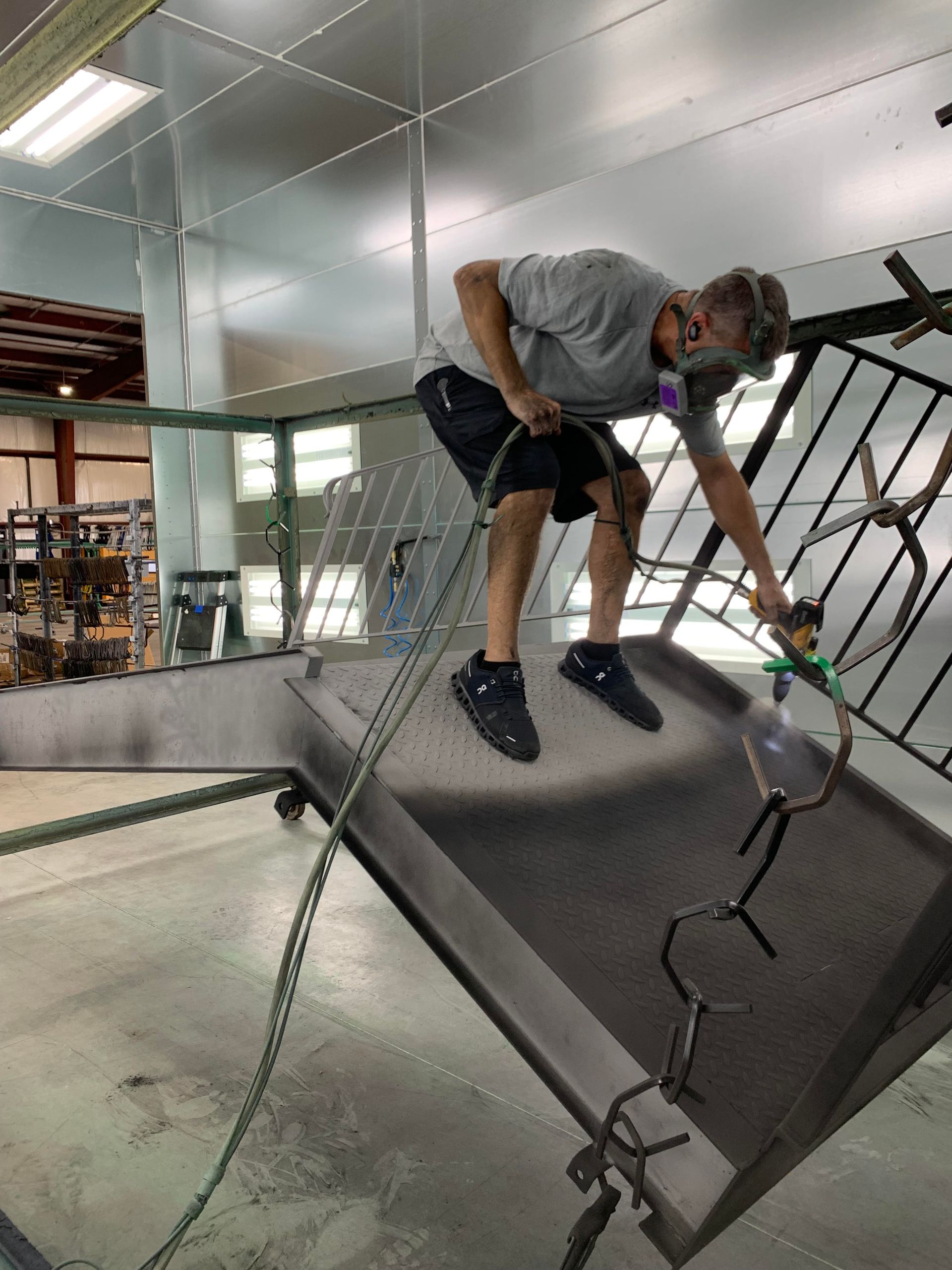 A man is spray painting a metal structure in a factory.