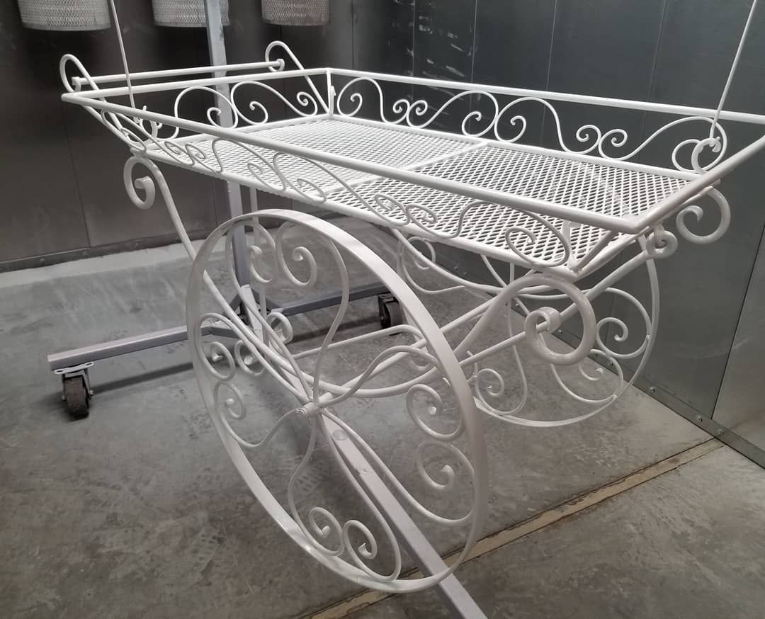 A white wrought iron cart with wheels is sitting on the ground.