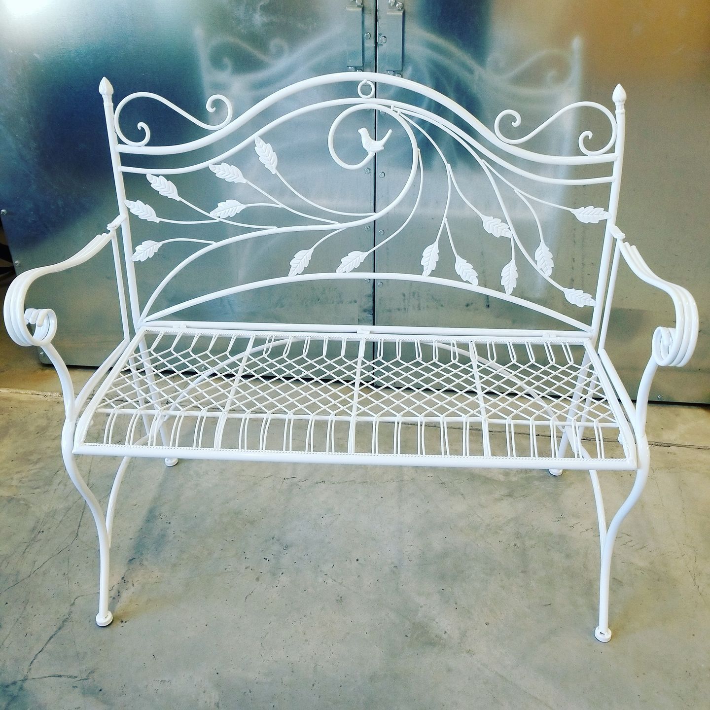 A white wrought iron bench with leaves on it