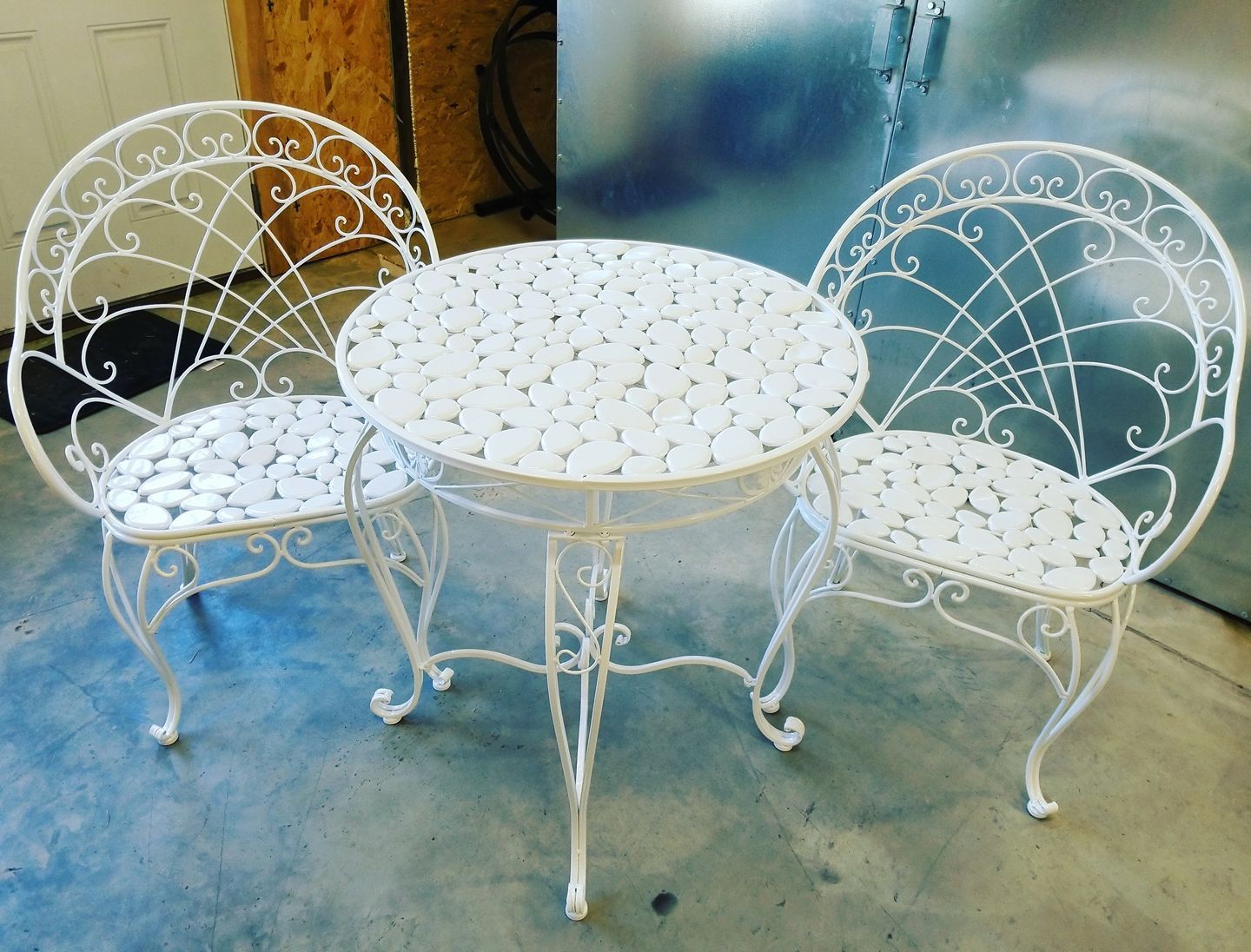 A white wrought iron table and chairs set on a concrete floor