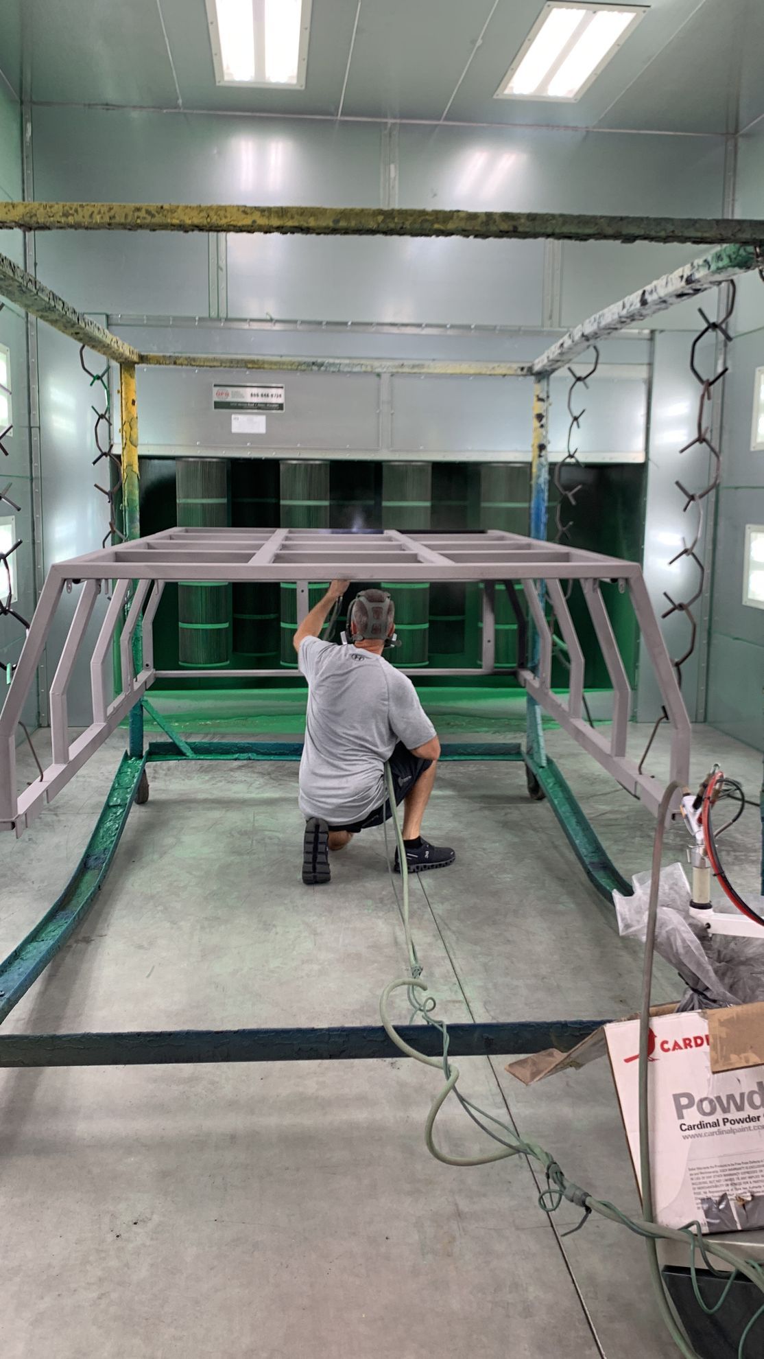 A man is kneeling down in a paint booth holding a piece of metal.