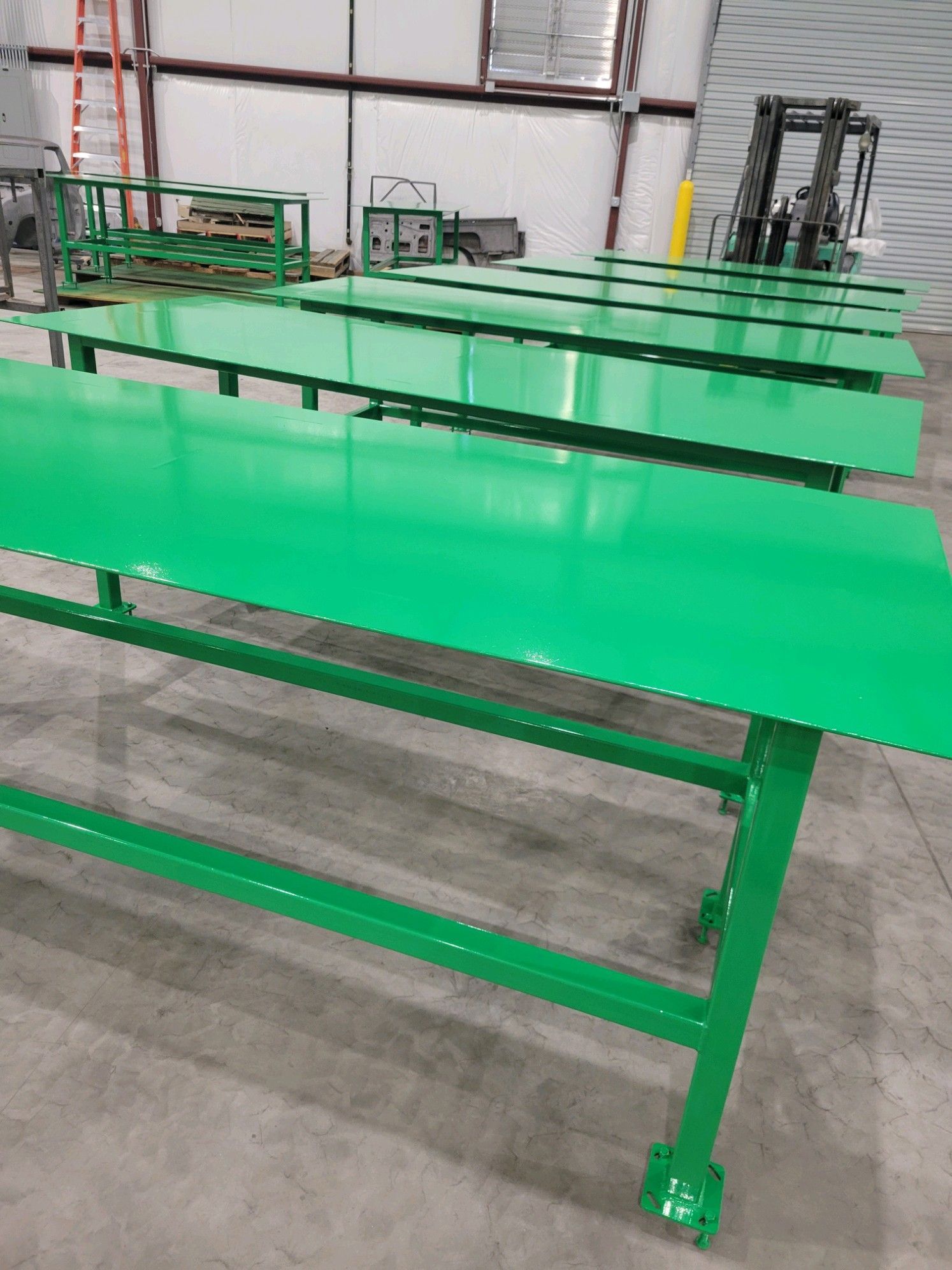 A row of green tables in a warehouse with a forklift in the background